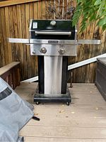 Front view of KitchenAid outdoor grill positioned on a deck, showing lid closed, wheels, and attached side shelves