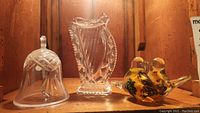 Photo of crystal bell, Waterford harp figurine, and two yellow and black glass bird figurines on wooden shelf