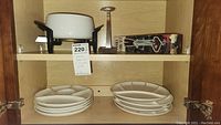 Shelf with white ceramic fondue pot in black metal stand on top shelf, set of eight white segmented plates below.