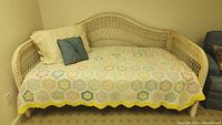Front view of wicker day bed, showing vintage quilt, white and blue pillows, mattress optional
