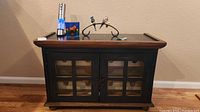 Front view of the wine cabinet showing the painted top, glass pane double doors, and accessories on top.