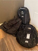 Four backpacks placed indoors on wooden floor, showing three The North Face backpacks and one ABC backpack in dark colors.