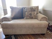 Front view of large beige upholstered chair with two pillows.