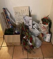 Overview of boxed Christmas decorations including wrapping supplies, garlands, and wall art leaning against the wall.