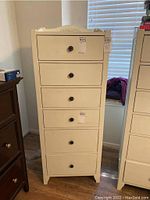 Front view of the tall white dresser showing six drawers and dark round knobs with a decorative top rail.