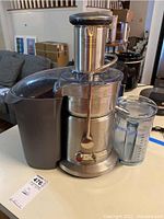 Front and side view showing juicer assembled with pulp container on left and clear measuring pitcher positioned at spout