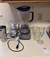 KitchenAid blender, Cuisinart mini prep plus, three glass jars and metal grater on counter, power cords visible