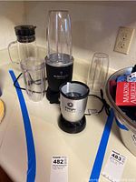 Full set photo showing Nutribullet Balance base, three blender cups, Magic Bullet blender base, and plastic drink pitcher with lid on kitchen counter.