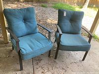 Two metal framed chairs with blue cushions on outdoor concrete surface, cushions tufted with buttons