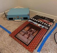 Blue Crosley portable phonograph and country music vinyl albums on carpeted floor near corner wall