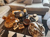 Photo showing Texas-shaped wood art sculpture, candleholders with candles, wooden bowls, cork figurines, cotton and jute runner, and some decorative accessories on a wooden coffee table.