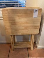 Three wooden tray tables leaning against a wall side by side, showing foldable legs and wood grain.
