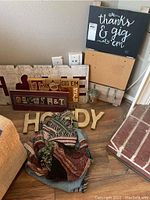 Overview of wooden signs arranged leaning on wall, metal HOWDY letters, and a folded Texas A&M patterned throw on floor