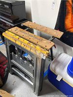 Photo of Sears Craftsman adjustable work table folded up resting against wall with two saw horses stacked