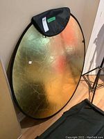 Full view of the round gold side of the backdrop leaning against the wall with the black carry case nearby.