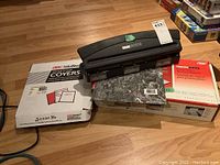 Wide view of the Docubind binding punch sitting on a box of BSC Velobind presentation covers with a box of presentation binding cones on the side.