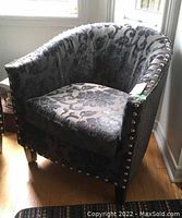 Front side angle of black velvet tub chair showing floral damask upholstery and metallic tack heads along the arm and back edges