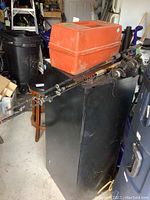 Overview showing two fishing rods and orange plastic tackle box on top of a black cabinet in a garage storage area.