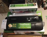 Photo showing FoodSaver V2244 vacuum sealer machine on top of box next to two rolls of heat seal bags.