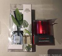 Lot overview showing Ocean Breeze reed diffuser in clear packaging with green leaves and fragrance label, next to red Blackweb Soundpebble wireless speaker in box.