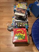 Top view of stacked board games and puzzles including Apples to Apples and a 1000-piece fantasy-themed puzzle on top.