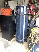 Full tall navy blue golf travel case standing upright among other golf equipment in a storage area.