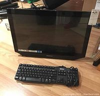 Photo showing black Hannspree monitor and black Dell wired keyboard placed on wooden floor.