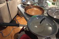 A selection of pans and lids on a table showing different materials and handle types