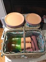 Top view of the woven picnic basket filled with dinner plates, salad plates, mugs, and drinking cups, showing peach and mauve color scheme and floral fabric lining.