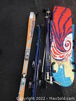 Full overview of the set including skis, ski poles, and snowboard in one image showing their relative size and color.
