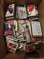 View inside the box showing various stacked and scattered sports cards, a mix of hockey and baseball with different styles and sizes, many sleeved.