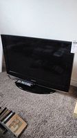 Samsung 32 inch LCD TV, black bezel, showing screen and base stand, remote control resting on base