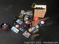 Overview of the group of tools arranged on ground showing hand saw, planes, voltmeter, sockets, tie downs, chain, wooden storage box, and various small tools