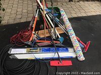 Assorted yard tools including rakes, shovels, brooms, extension cords, and a wrapped beach umbrella.