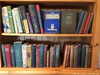 Photo showing two wooden shelves of vintage books with various bindings and titles like 'Eliza Cook','Trinity', and others.
