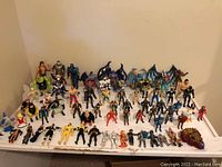 Wide shot showing 68 assorted action figures of multiple types standing on a white surface against beige background.