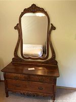 Full front view of the antique dresser with attached large decorative mirror showing the wood grain and ornate frame.