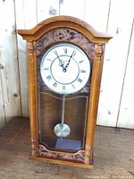 Front view of the wooden Bulova wall chime clock showing the dial, pendulum, and columns.