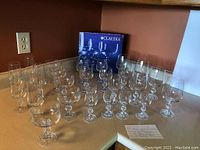 Multiple Claudia crystal stemware glasses of various shapes and sizes arranged on kitchen countertop with branding box behind