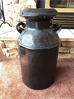 Straight-on image of the black metal milk can with visible handles and embossed text.