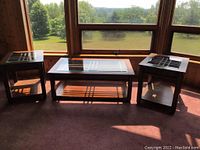 Photo showing two matching end tables and one coffee table with glass tops placed by a window.