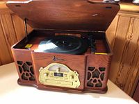 Front angled view of the Emerson wooden record player with top lid open showing the vinyl turntable inside, two speaker grilles on either side, and gold-tone radio control panel on front.