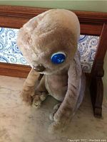 Front side of ET plush figure showing large blue eyes and brown nose, seated position.