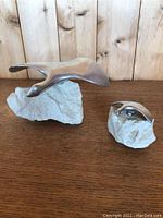 Two pewter Hoselton sculptures mounted on light gray natural stone bases, shown side by side on wooden surface with wood panel background.