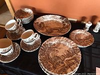 Display of Johnson Brothers Cotswold cups, saucers, dinner plates, bread plates, dessert plates, serving tray with rustic scenic prints.