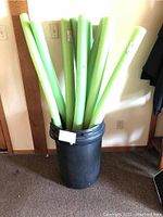 Ten green foam pool noodles standing upright in a black bucket.