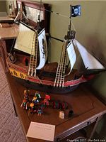 Full view of Playmobil pirate ship with sails and rigging showing Jolly Roger flag, figures, cannons, sack, barrel on table.