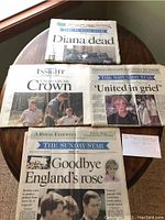 Four newspapers laid out on a round wooden table showing headlines and images related to Princess Diana's death and funeral.
