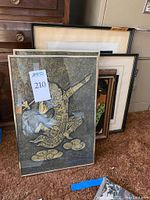 Five framed pieces of Asian wall art stacked against the wall, showing intricate gold textured designs and framed matting.