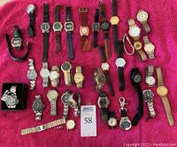 Overview of thirty-eight men's wristwatches arranged on a pink fabric background showing various styles, bands, and dial colors.